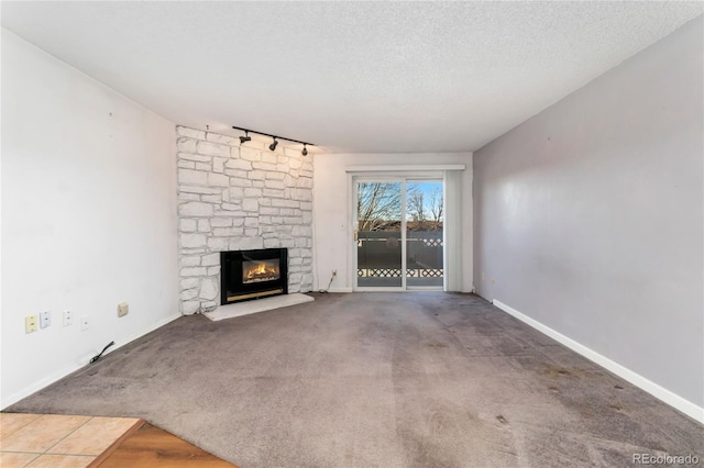 unfurnished living room featuring a stone fireplace, carpet flooring, a textured ceiling, and baseboards