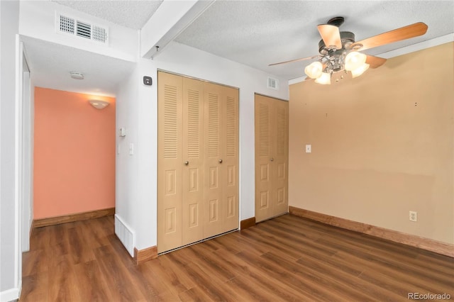 unfurnished bedroom featuring visible vents, a textured ceiling, baseboards, and wood finished floors