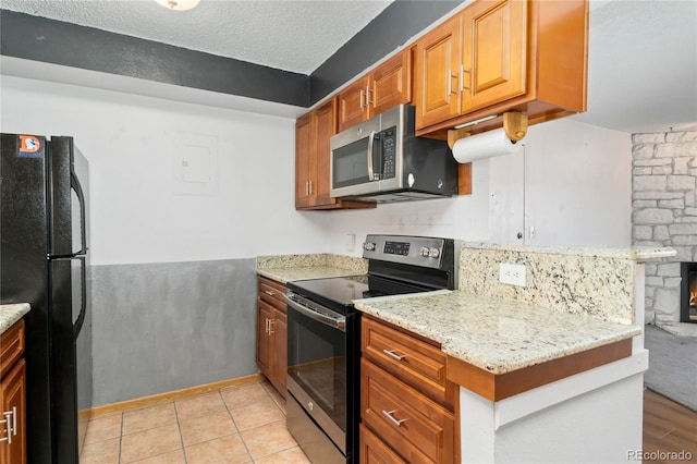 kitchen featuring light stone countertops, light tile patterned flooring, stainless steel appliances, a textured ceiling, and brown cabinets