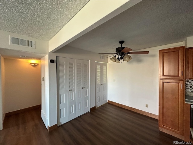 unfurnished bedroom with a textured ceiling, dark wood finished floors, baseboards, visible vents, and a ceiling fan