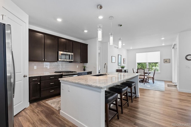 15802 Xanthia Way, Thornton, CO 80602 - kitchen with stainless steel appliances, a kitchen bar, dark brown cabinetry, light wood-type flooring, and backsplash
