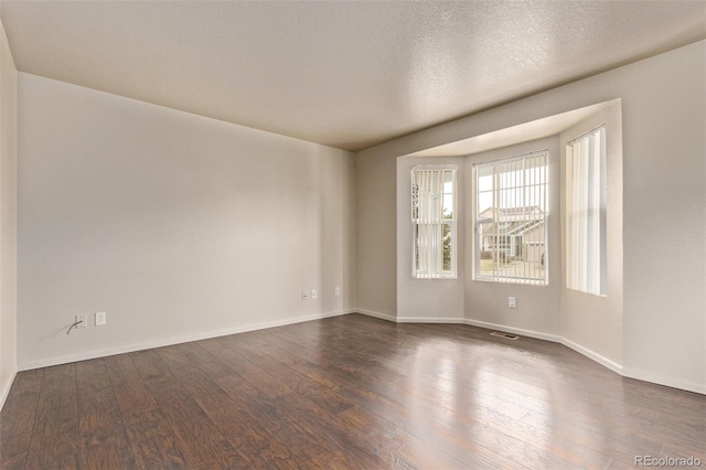 spare room featuring a textured ceiling, baseboards, and dark wood finished floors