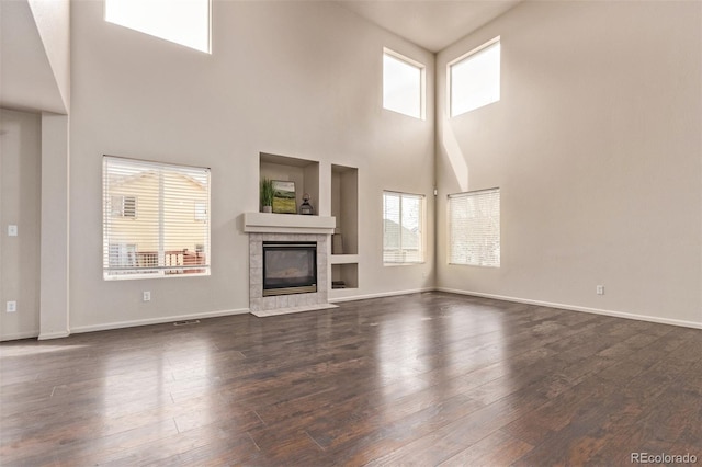 unfurnished living room with dark wood-style floors, a tile fireplace, and baseboards