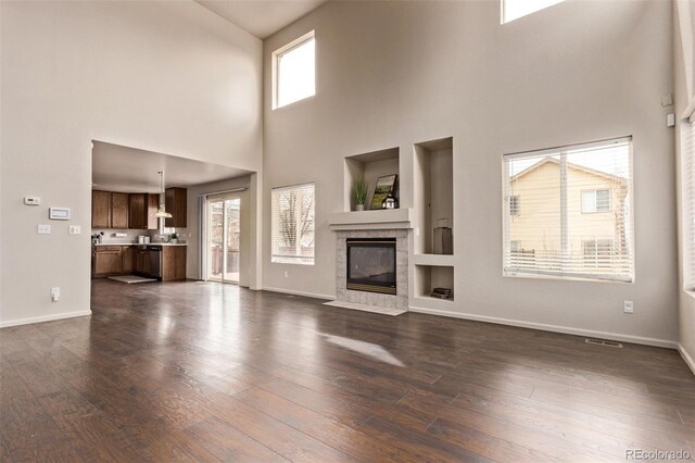 unfurnished living room featuring a tile fireplace, plenty of natural light, and dark wood finished floors