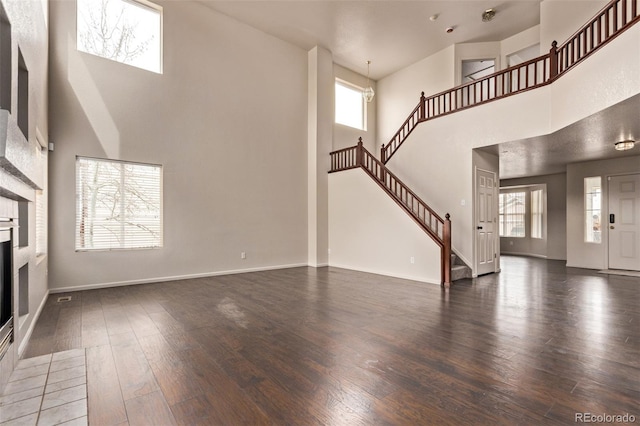 entryway with stairway, baseboards, a high ceiling, a tiled fireplace, and wood finished floors