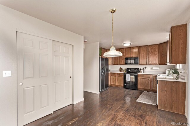 kitchen with light countertops, pendant lighting, dark wood-style floors, brown cabinetry, and black appliances