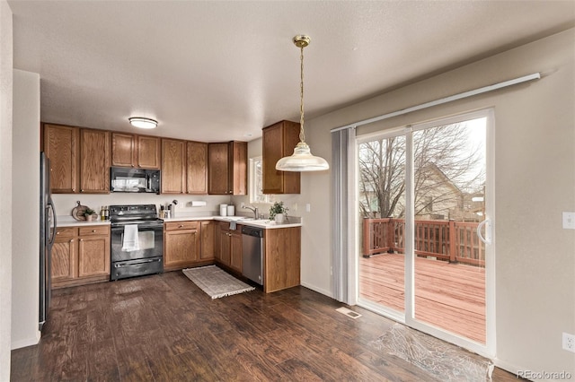 kitchen featuring light countertops, decorative light fixtures, brown cabinets, dark wood-style floors, and black appliances