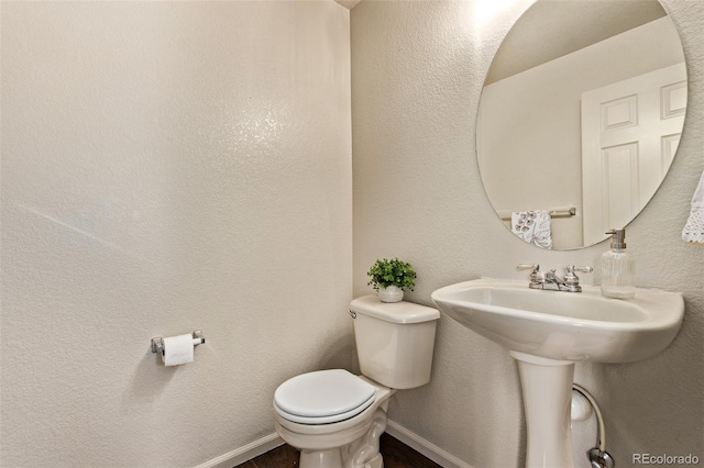 half bathroom with baseboards, toilet, and a textured wall