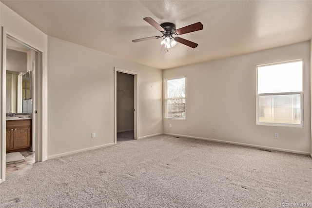 unfurnished bedroom featuring ensuite bathroom, baseboards, a walk in closet, and carpet flooring