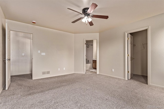 unfurnished bedroom with a walk in closet, carpet, ensuite bath, ceiling fan, and visible vents