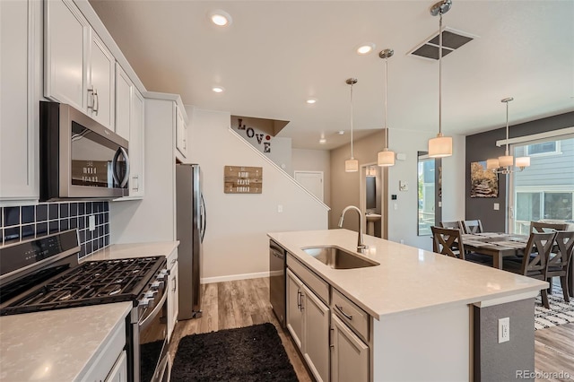 kitchen featuring stainless steel appliances, a sink, light wood-style flooring, an island with sink, and decorative backsplash