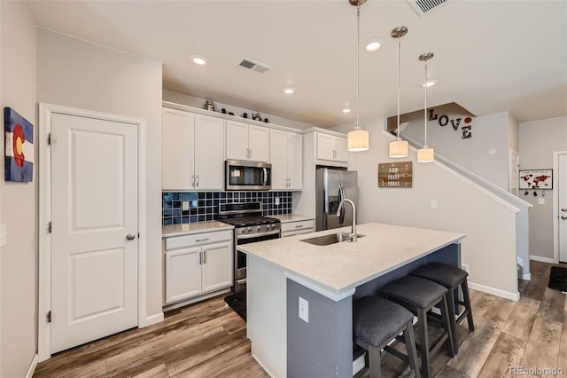 kitchen with appliances with stainless steel finishes, a sink, a kitchen breakfast bar, a center island with sink, and white cabinetry