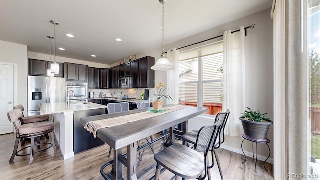 kitchen with dark brown cabinetry, decorative backsplash, appliances with stainless steel finishes, decorative light fixtures, and a kitchen bar