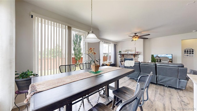 dining room with a ceiling fan, light wood-type flooring, and a stone fireplace