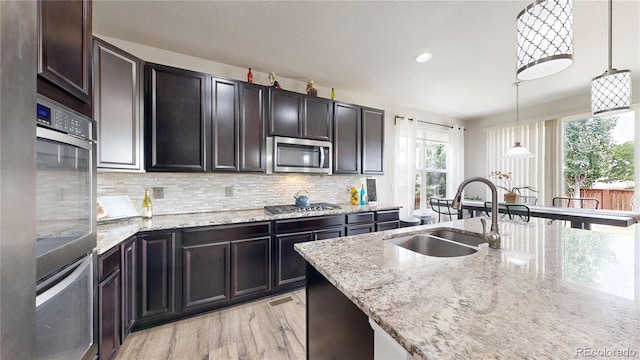 kitchen featuring light stone counters, appliances with stainless steel finishes, a sink, and decorative light fixtures