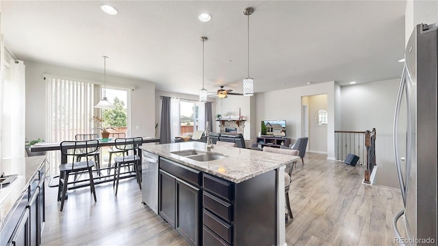 kitchen with stainless steel appliances, a sink, hanging light fixtures, and an island with sink