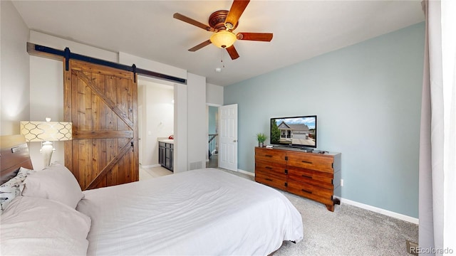 bedroom featuring a barn door, baseboards, a ceiling fan, light colored carpet, and ensuite bath