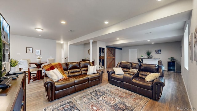 living room featuring a barn door, visible vents, light wood-style flooring, stairway, and recessed lighting