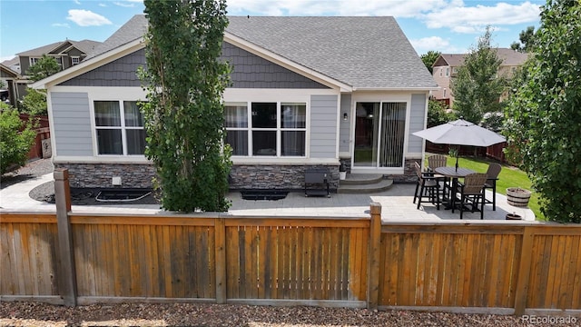 back of house with entry steps, stone siding, a fenced backyard, and a patio