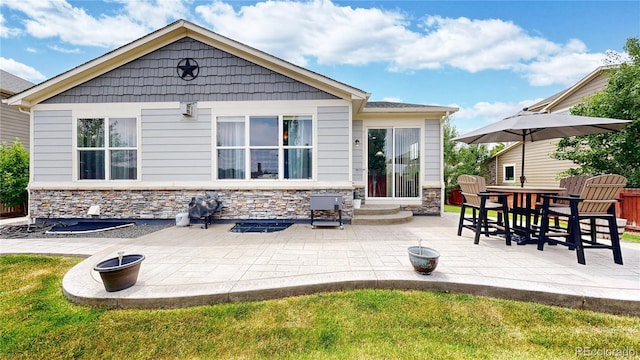 rear view of house with entry steps, stone siding, a patio area, and a lawn