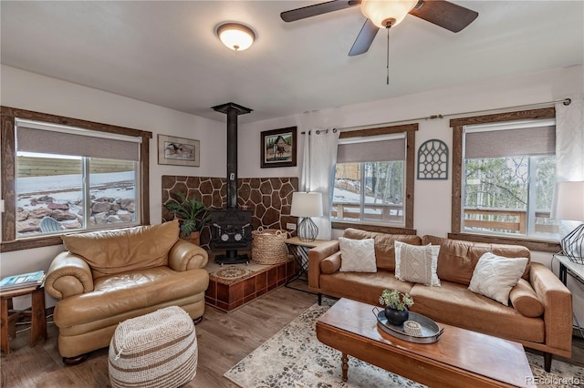 living room featuring a wood stove, ceiling fan, and wood finished floors