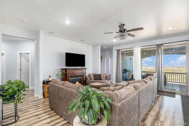 living room with light wood-type flooring, a glass covered fireplace, and recessed lighting