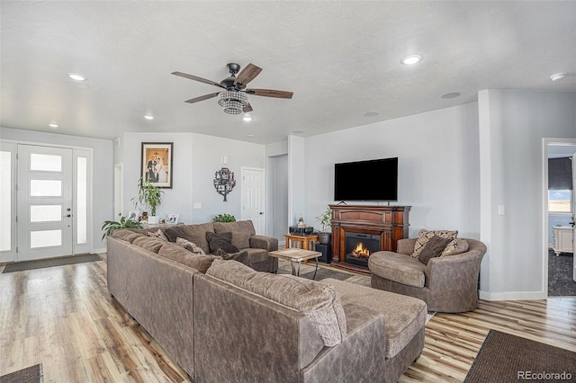 living room featuring light wood-type flooring, a warm lit fireplace, a healthy amount of sunlight, and recessed lighting