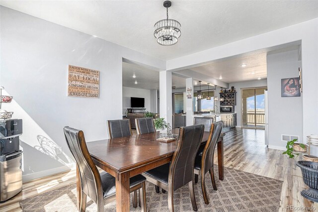 dining space with baseboards, light wood-type flooring, visible vents, and a notable chandelier