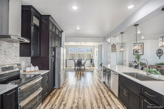 kitchen featuring light wood finished floors, wall chimney exhaust hood, a sink, stainless steel appliances, and backsplash