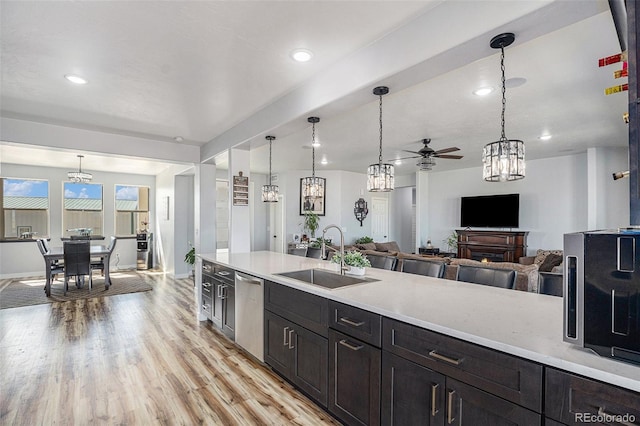 kitchen with light countertops, light wood-style floors, open floor plan, a sink, and dishwasher