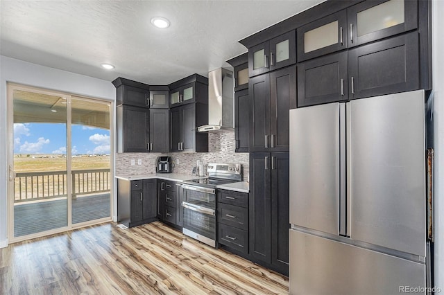 kitchen featuring stainless steel appliances, light countertops, backsplash, wall chimney range hood, and light wood-type flooring