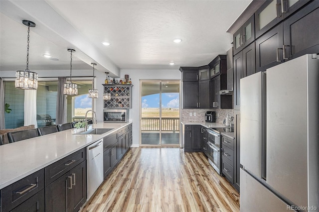 kitchen with stainless steel appliances, decorative backsplash, light wood-style floors, glass insert cabinets, and a sink