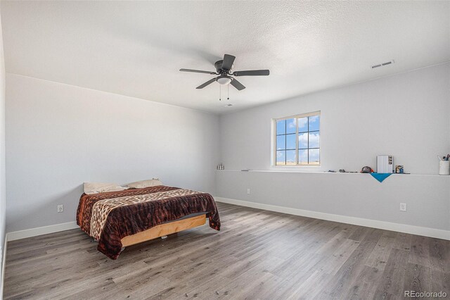 bedroom featuring visible vents, ceiling fan, a textured ceiling, wood finished floors, and baseboards