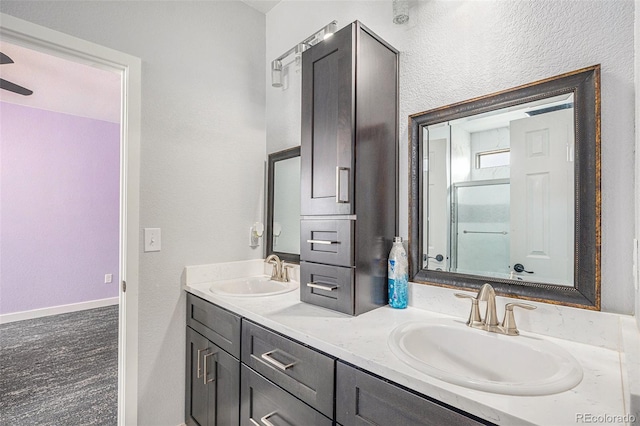 full bath featuring a shower with door, a sink, baseboards, and double vanity