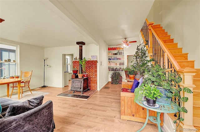living room featuring ceiling fan, wood finished floors, stairway, a wood stove, and baseboards