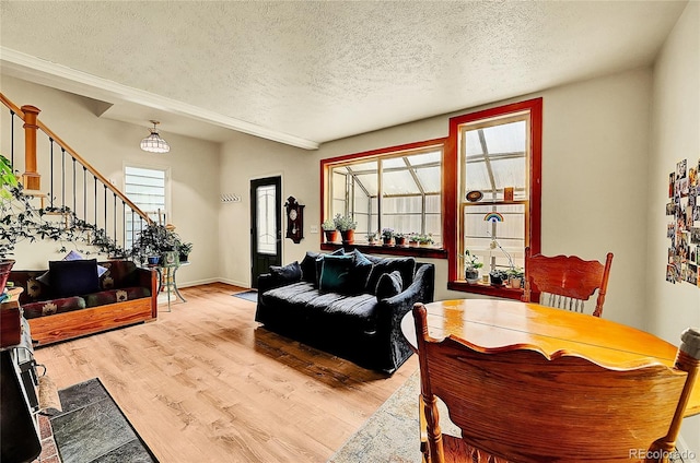living room featuring a textured ceiling, stairway, light wood-style flooring, and baseboards