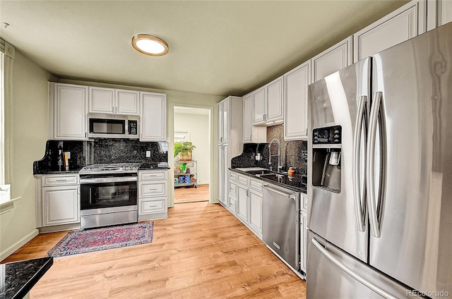 kitchen with appliances with stainless steel finishes, a sink, backsplash, and light wood-style floors