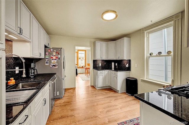 kitchen with a sink, light wood-type flooring, appliances with stainless steel finishes, tasteful backsplash, and dark stone counters