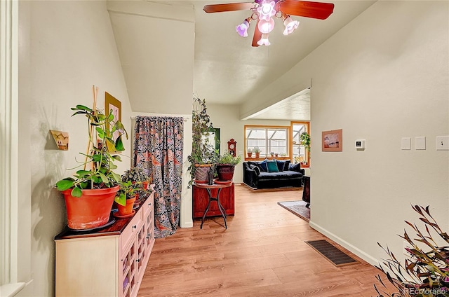 corridor featuring light wood-style flooring, vaulted ceiling, and baseboards