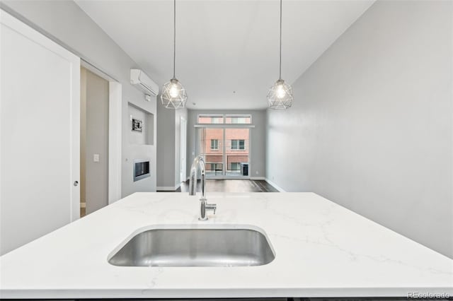 kitchen with an island with sink, sink, a wall unit AC, and decorative light fixtures