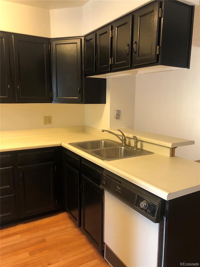 kitchen with light wood-type flooring, a sink, dark cabinetry, white dishwasher, and light countertops