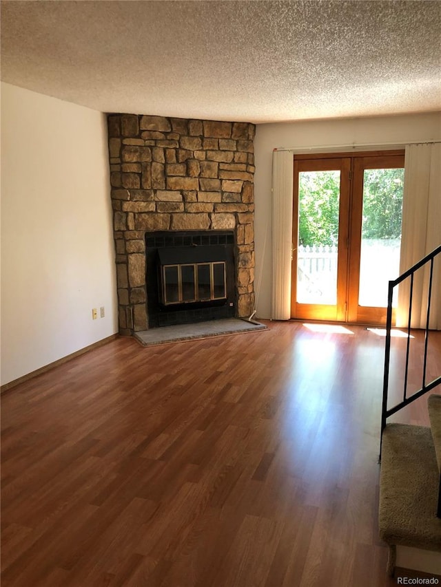 unfurnished living room featuring a fireplace, a textured ceiling, stairs, and wood finished floors