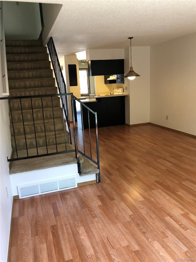 staircase with baseboards, wood finished floors, visible vents, and a textured ceiling