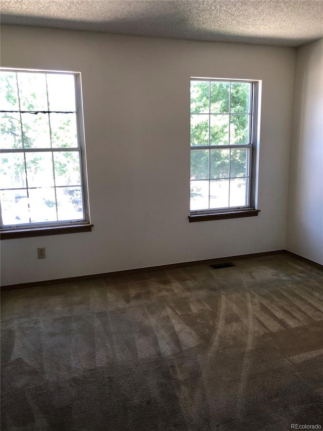 unfurnished room with dark colored carpet, visible vents, and a textured ceiling