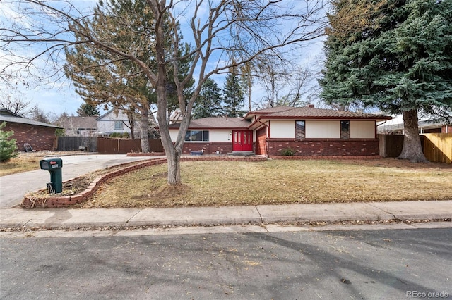 ranch-style home with concrete driveway, brick siding, fence, and a front lawn