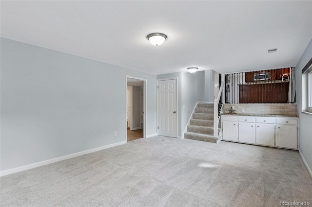 unfurnished living room featuring baseboards, stairs, visible vents, and light colored carpet