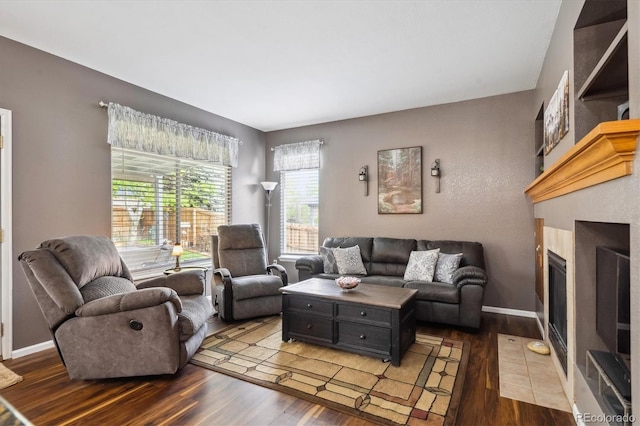 living area featuring baseboards, a fireplace with flush hearth, and wood finished floors