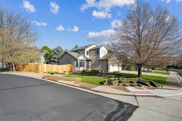 traditional-style home with fence, a front yard, solar panels, and a garage