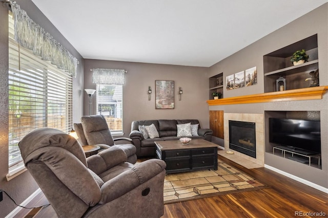 living area featuring baseboards, a fireplace, wood finished floors, and built in shelves