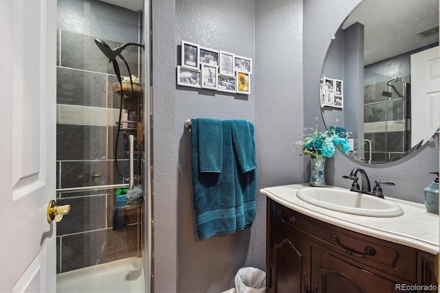 full bathroom with vanity, a textured wall, visible vents, and a stall shower